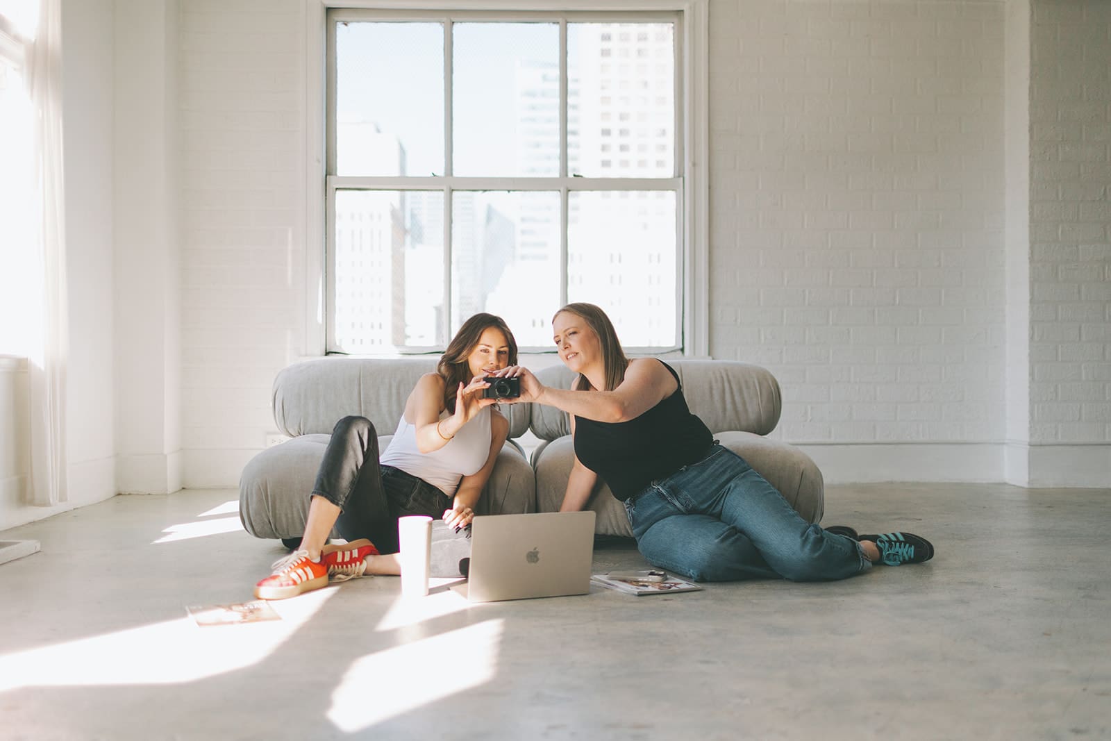 girls sitting on ground in a neutral studio with a laptop and camera researching how to repurpose her instagram content to TikTok